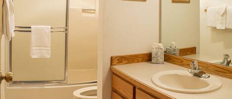 A bathroom with a shower, toilet, sink, and mirror.