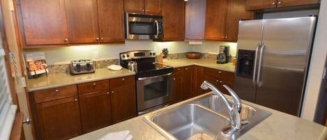 A modern kitchen with wooden cabinets, stainless steel appliances, a double sink, and a granite countertop.