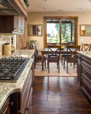 A kitchen with a central island, wooden cabinets, and a dining area with a table and chairs. - Lakeside Caldera Retreat with Access to Forest House (Bend)