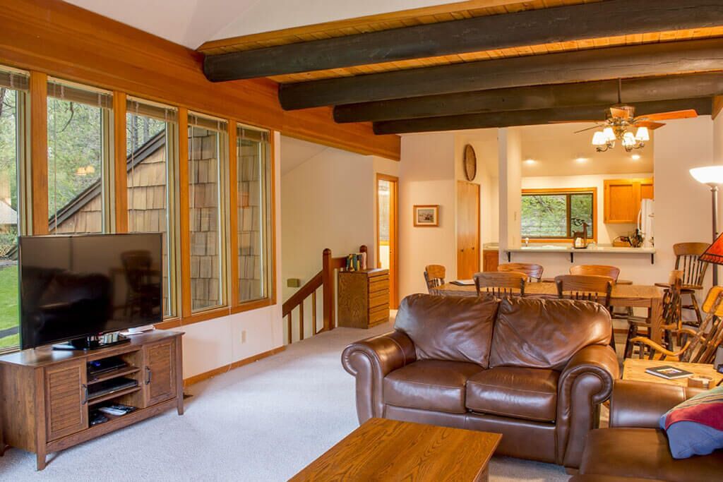 A spacious living room with a leather sofa, wooden entertainment unit, and large windows.