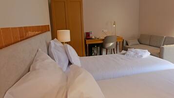A hotel room with two beds, a desk with a lamp, a chair, and a sofa.