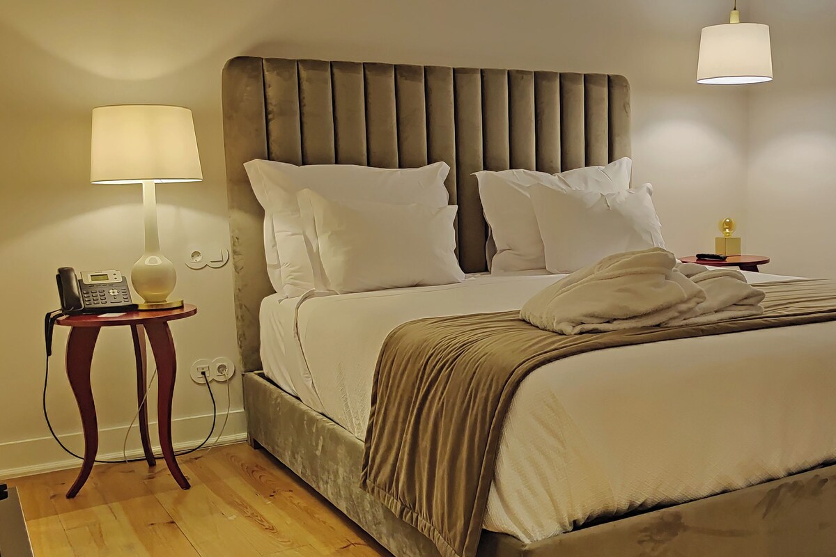 A neatly made bed with a headboard, a bedside table with a lamp, and a telephone.