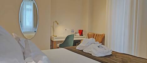 A hotel room with a bed, a desk, a chair, a mirror, and a window with curtains.