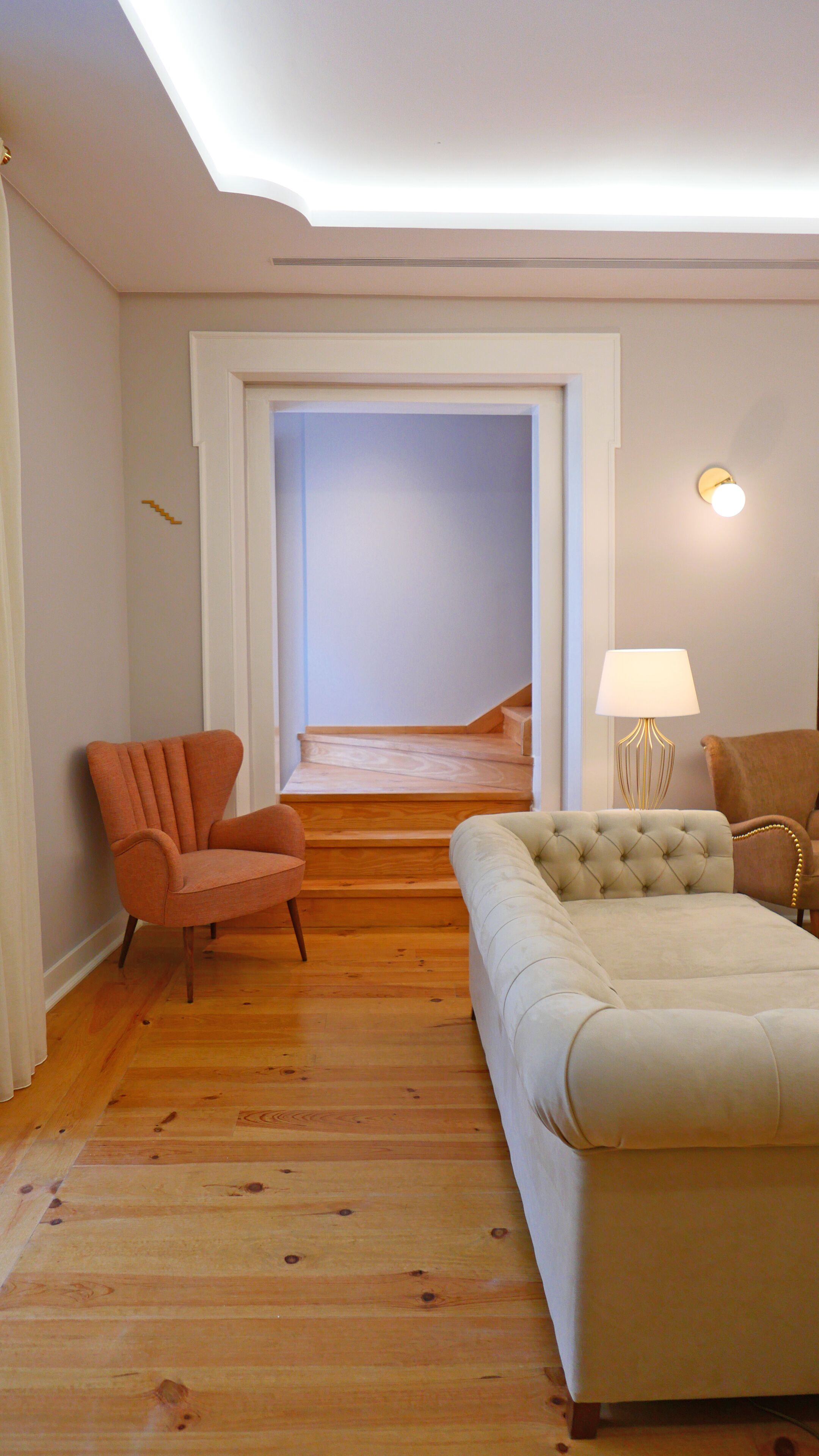 Una sala de estar con piso de madera, un sofá color beige, un sillón marrón y una lámpara.