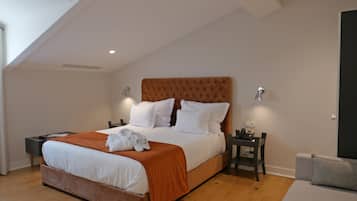 A neatly made bed with white linens and an orange throw blanket, a bedside table with a lamp, and a small nightstand with a phone.