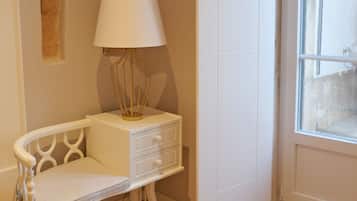 Une chambre d’angle avec une chaise blanche, une petite table de chevet avec une lampe, un plancher en bois et une fenêtre donnant sur un beau paysage.
