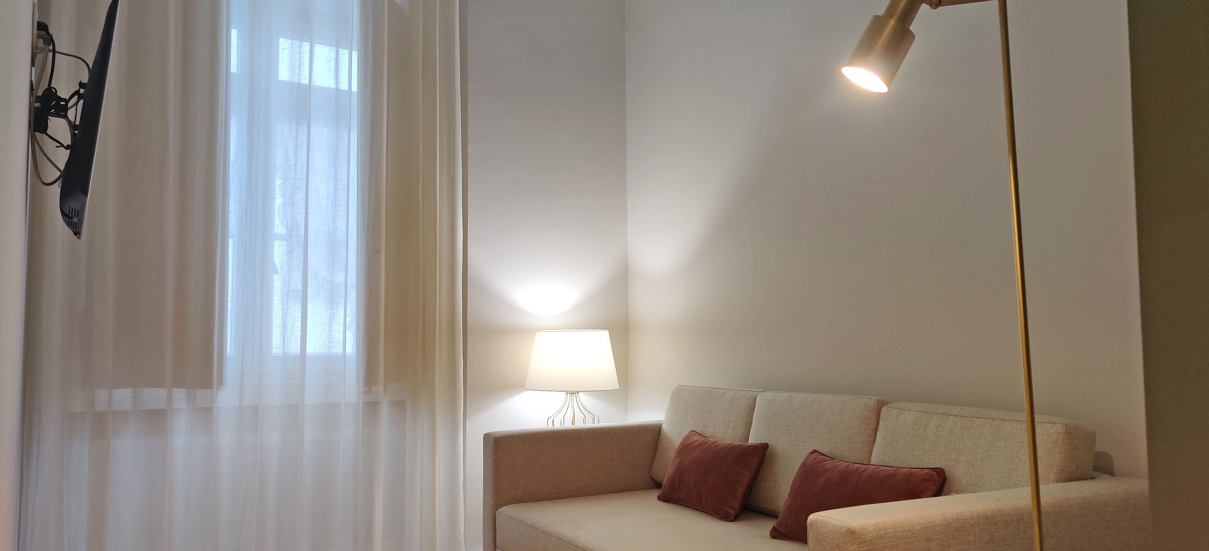 Una habitación con sofá, lámpara y ventana con cortinas traslúcidas.