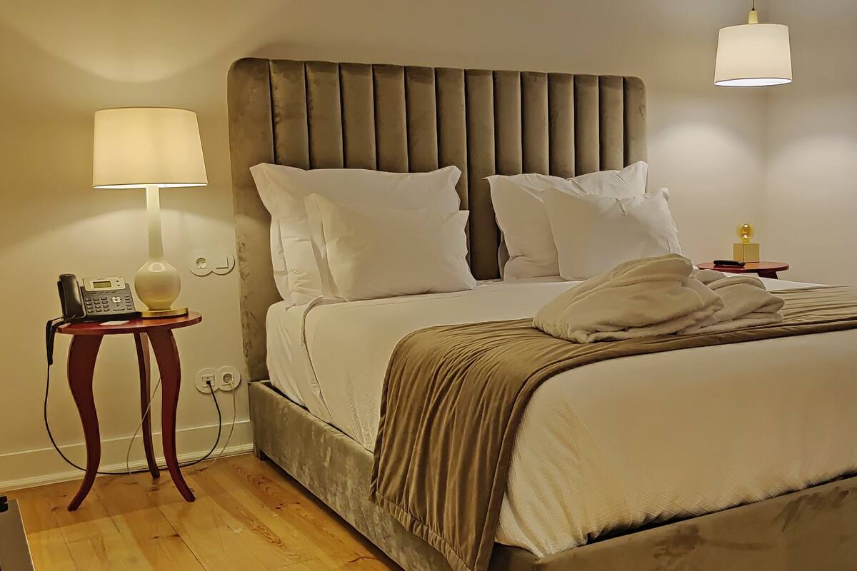 A neatly made bed with a headboard, a bedside table with a lamp, and a telephone.