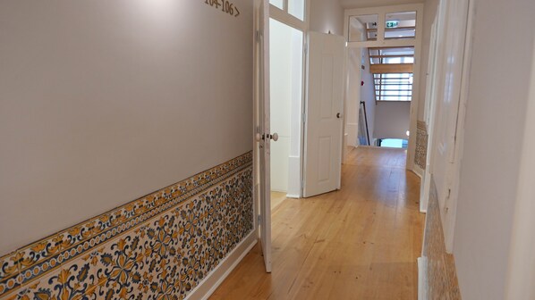 A hallway with patterned tile flooring, white walls, and a wooden door. - Casa dos Ofícios Hotel (Tomar)