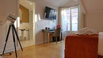 Ett hotellrum med en säng, ett skrivbord, en stol, en tv och ett stativ.