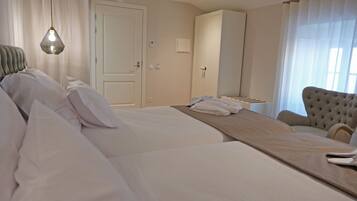 A hotel room with a large bed, a chair, a wardrobe, and a hanging light fixture.