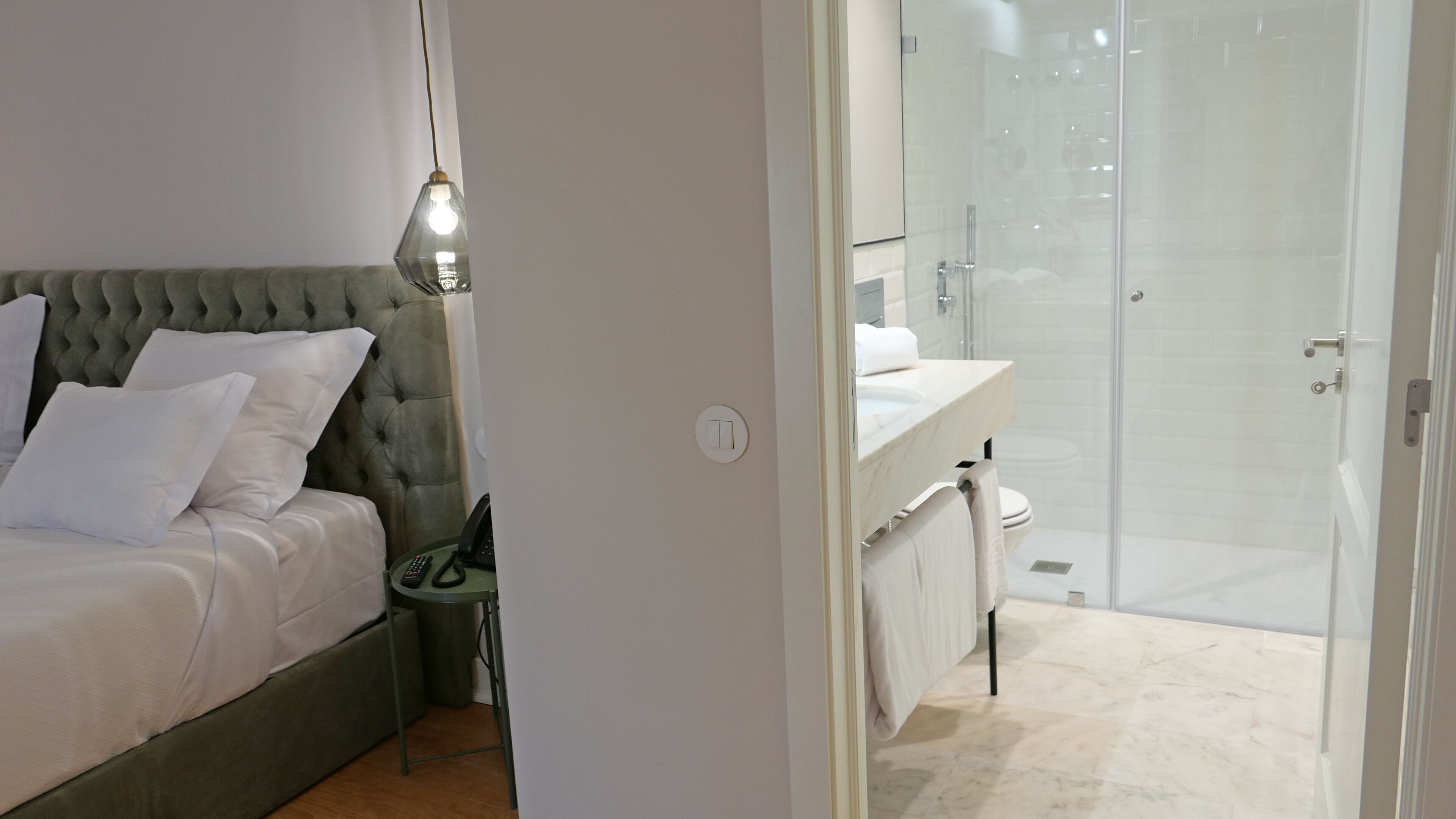 A bedroom with a bed, bedside table, and a hanging light fixture.