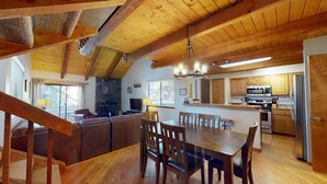 A cozy, rustic interior with a wooden ceiling, a stone fireplace, a dining area with a wooden table and chairs, and a kitchen with modern appliances. - Tennis Village Escape with Access to The Cove (Sunriver)