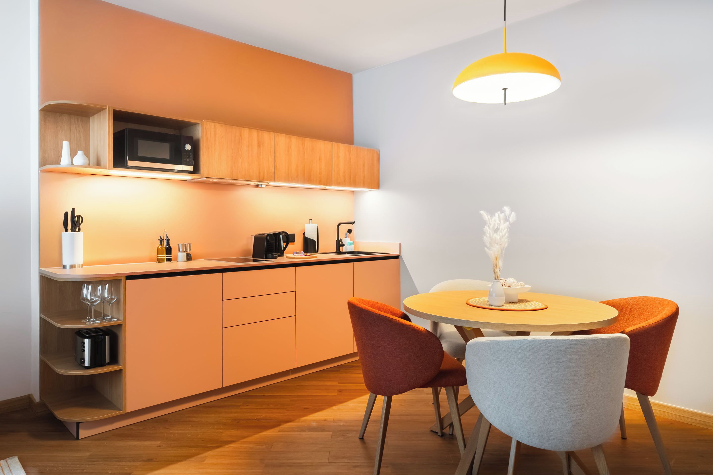 Una cocina moderna con microondas, tostadora y cafetera, una mesa de comedor con sillas e iluminación colgante.