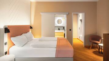 A modern hotel room with a large bed, a bedside table, a chair, and a bathroom visible through an open door.