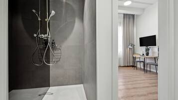 A modern bathroom with a shower, a toilet, and a sink. There is a dining area with a table and chairs visible through an open doorway.
