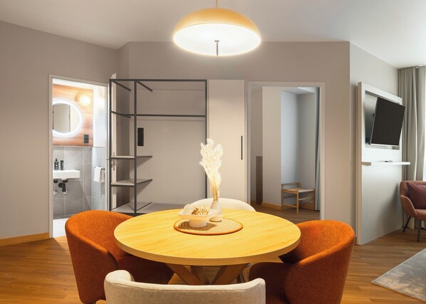 A modern living room with a round wooden table, orange chairs, a standing lamp, and a TV mounted on the wall. - Limehome Munich Fritz-Erler Str. (Munich)
