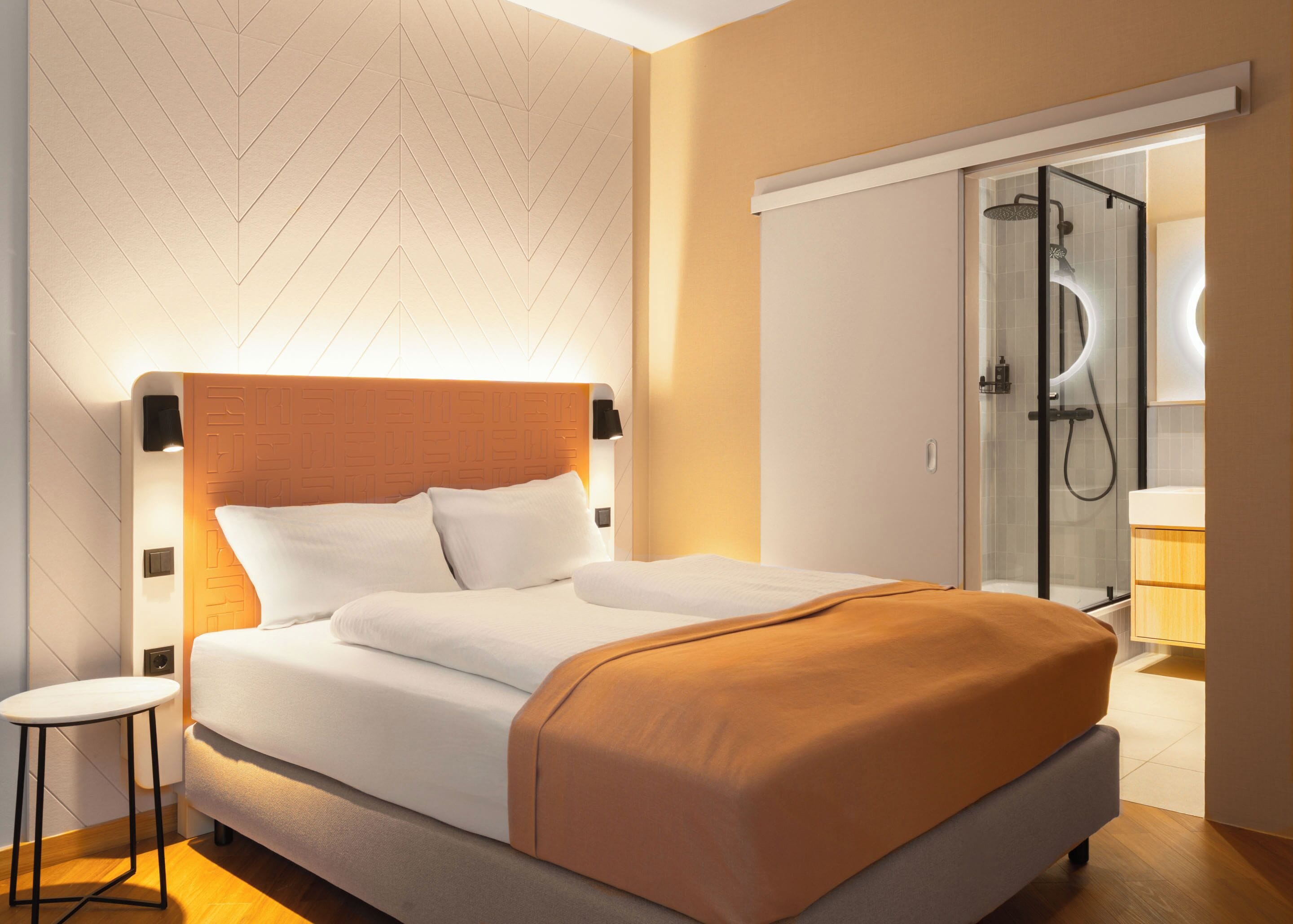 Een moderne hotelkamer met een bed, een klein tafeltje, een inloopdouche en een kledingkast.