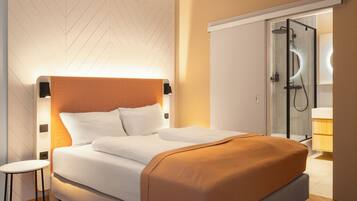 Een moderne hotelkamer met een bed, een klein tafeltje, een inloopdouche en een kledingkast.