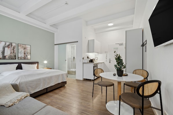 A modern hotel room with a bed, a small kitchenette, a dining area with a table and chairs, and a TV mounted on the wall. - Limehome Munich Fritz-Erler Str. (Munich)