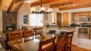 Un comedor amplio con una mesa y sillas de madera, una chimenea de piedra y una cocina con armarios de madera y electrodomésticos modernos.