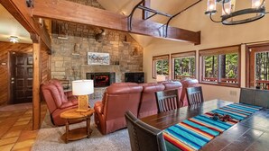 A cozy living room with a stone fireplace, leather seating, and a dining area with a colorful runner.
