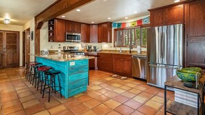 A spacious kitchen with wooden cabinets, a central island with stools, a stainless steel refrigerator, and a microwave.