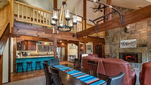 A spacious living area with a wooden dining table, red leather sofas, and a stone fireplace.