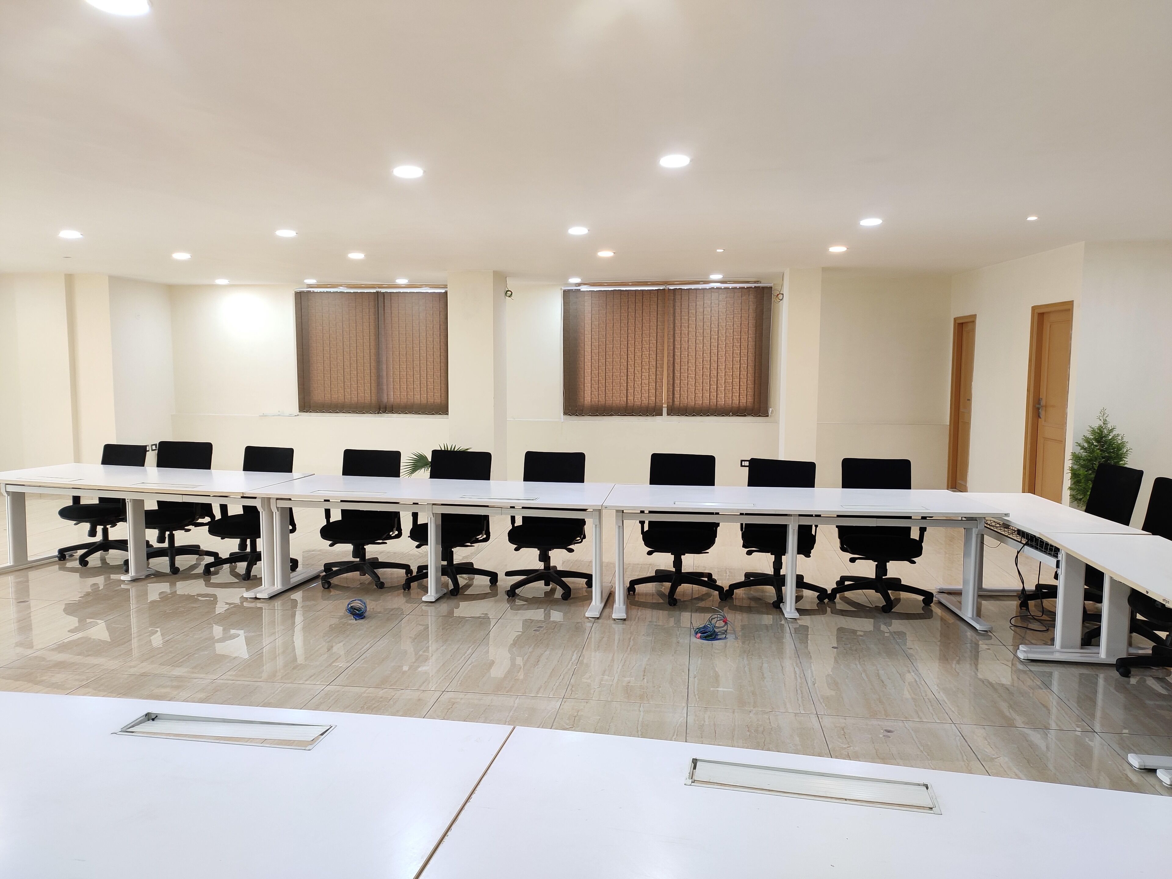 A conference room with a long table, black office chairs, and two windows with blinds.
