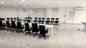 Un salón de conferencias con varias mesas y sillas, unidades de aire acondicionado y una pizarra.