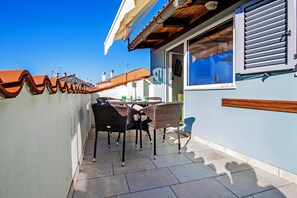 A patio with wicker chairs and a table, a tiled floor, and a building with a blue wall and a wooden ceiling.