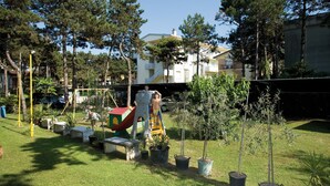Un espace de jeux avec un toboggan et des structures d’escalade, entouré de plantes en pot et d’arbres.