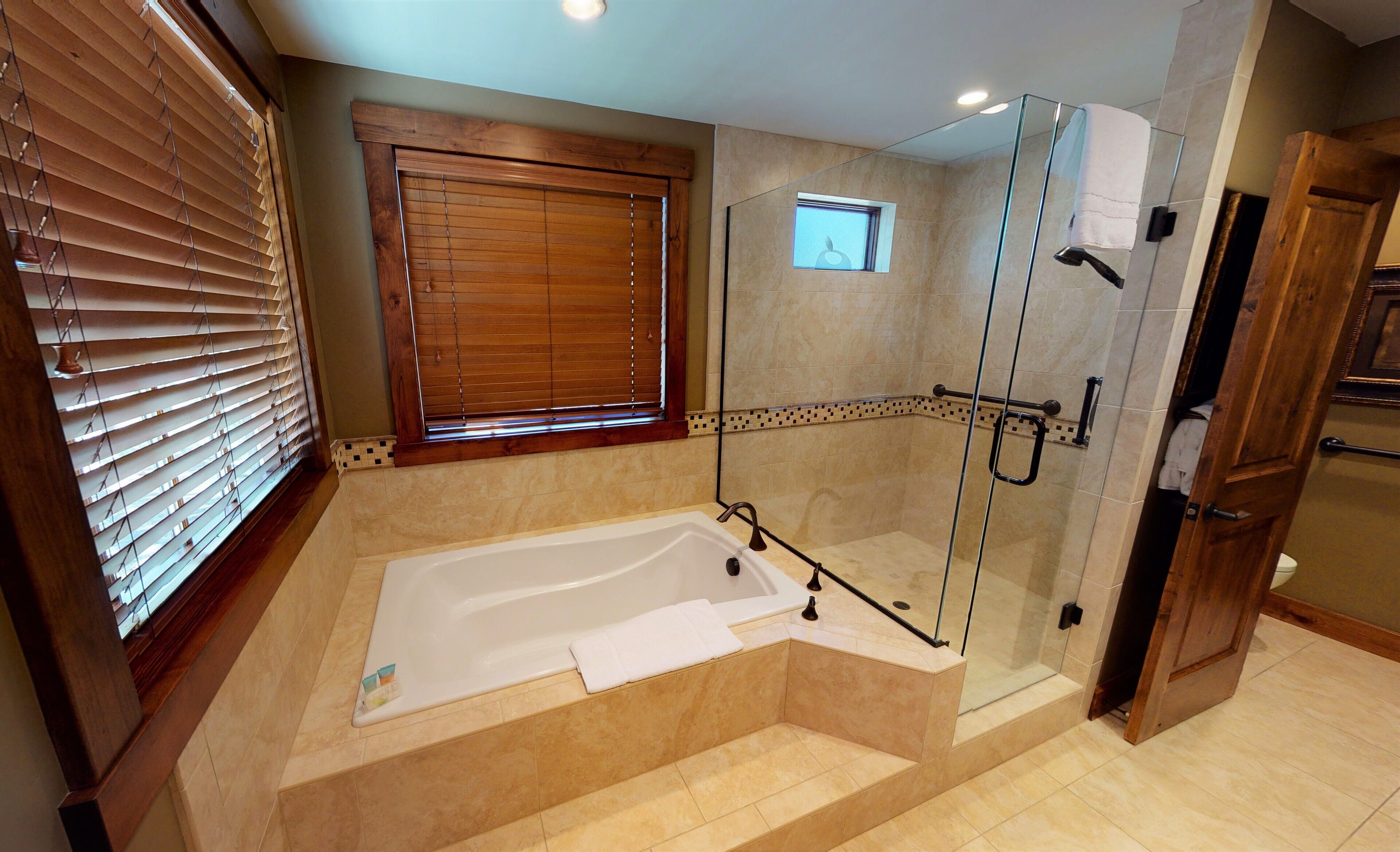Un baño moderno con ducha envuelta en vidrio, bañera independiente y ventana con persianas de madera.