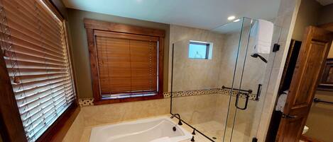 Un baño moderno con ducha envuelta en vidrio, bañera independiente y ventana con persianas de madera.