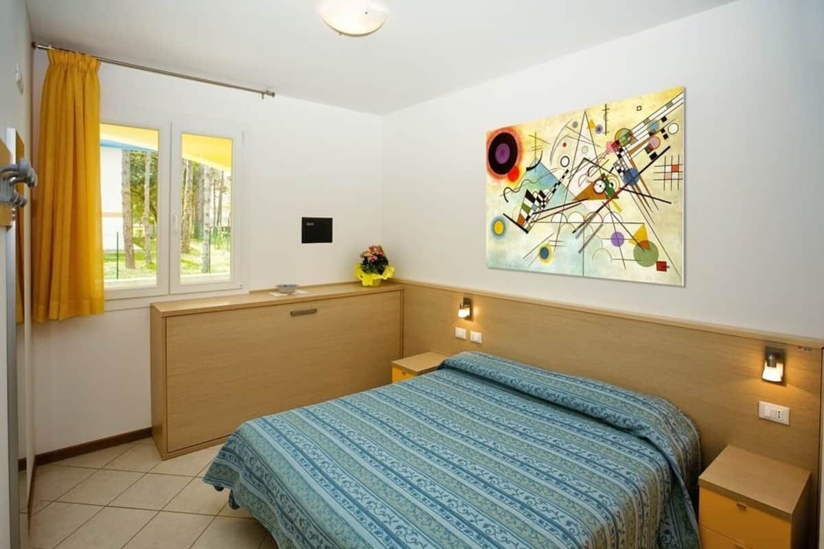 A bedroom with a bed, a window with curtains, a wall-mounted artwork, and bedside lamps.
