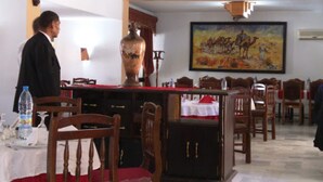 A dining area with wooden chairs, a table with a red tablecloth, a large vase, and a painting on the wall. - Hotel Antar Bechar (Bechar)