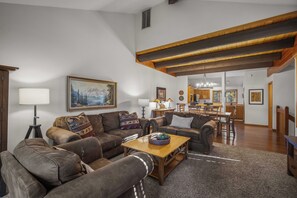 A spacious living room with a large brown leather sofa, a wooden coffee table, and a painting of a mountain landscape. - Wildflower Getaway with Access to Exclusive Golf (Bend)