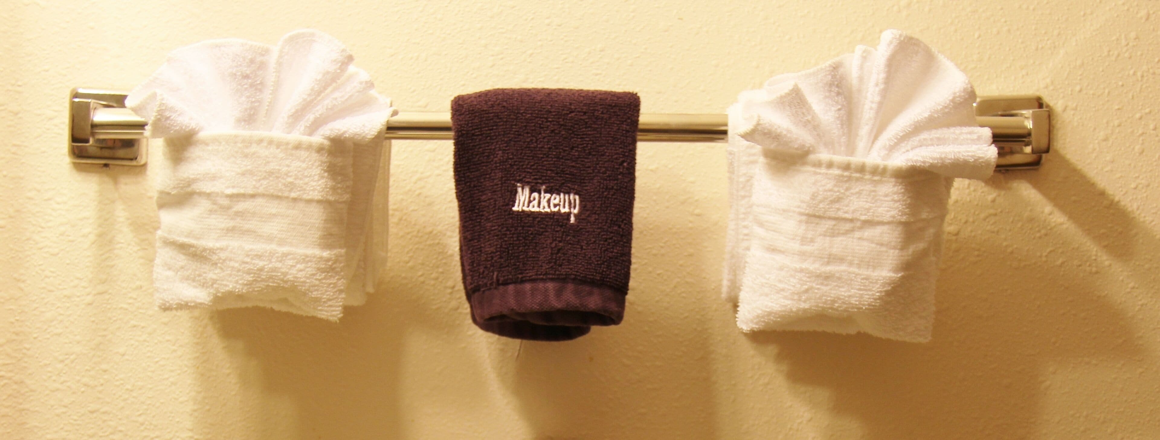 Un baño con dos toallas blancas colgadas en un perchero y una toalla marrón con la palabra 'Makeup' escrita.