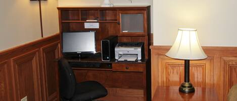 A wooden desk with a computer, printer, and lamp. There is a chair and a plant on the desk.