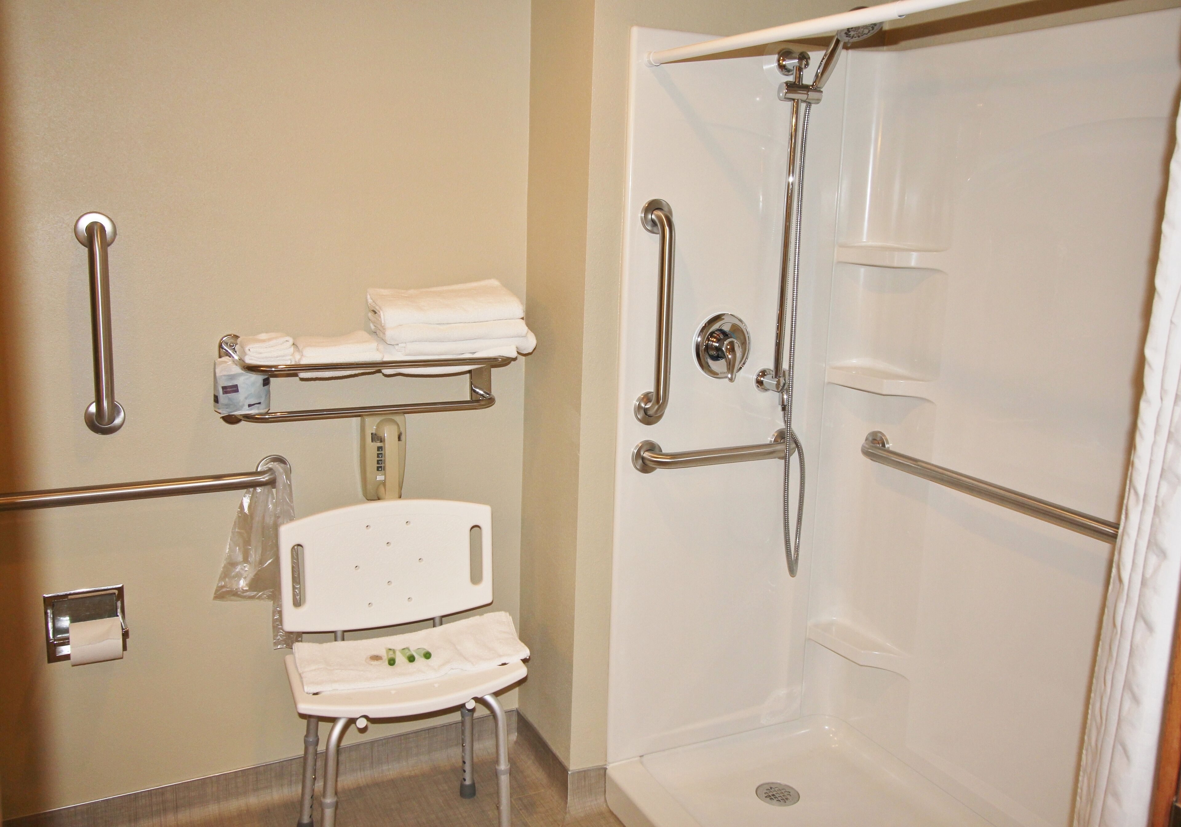 Un baño con ducha, barras de apoyo, un banco accesible para sillas de ruedas y un perchero para toallas.