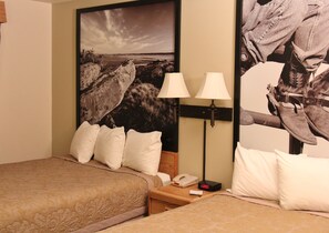 Habitación de hotel con dos camas, una mesita de noche con lámpara, teléfono y reloj digital.