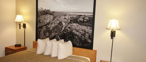 A hotel room with a large bed, two bedside tables, a nightstand, and a large framed picture on the wall.