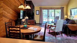 A cozy living room with a fireplace, wooden walls, and a large window offering a view of the outdoors. - Marina Access Retreat with Access to The Cove (Bend)