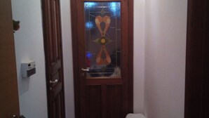 A narrow hallway with a wooden door, a small trash bin, and an air conditioning unit on the wall. - B&B Villa Mirella (Pachino)