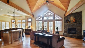 A spacious living area with a high ceiling, wooden beams, a stone fireplace, and large windows. - Caldera Lodge with Access to Exclusive Golf (Bend)