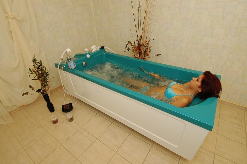 A woman relaxing in a bathtub with a blue interior, surrounded by decorative plants and a white curtain.