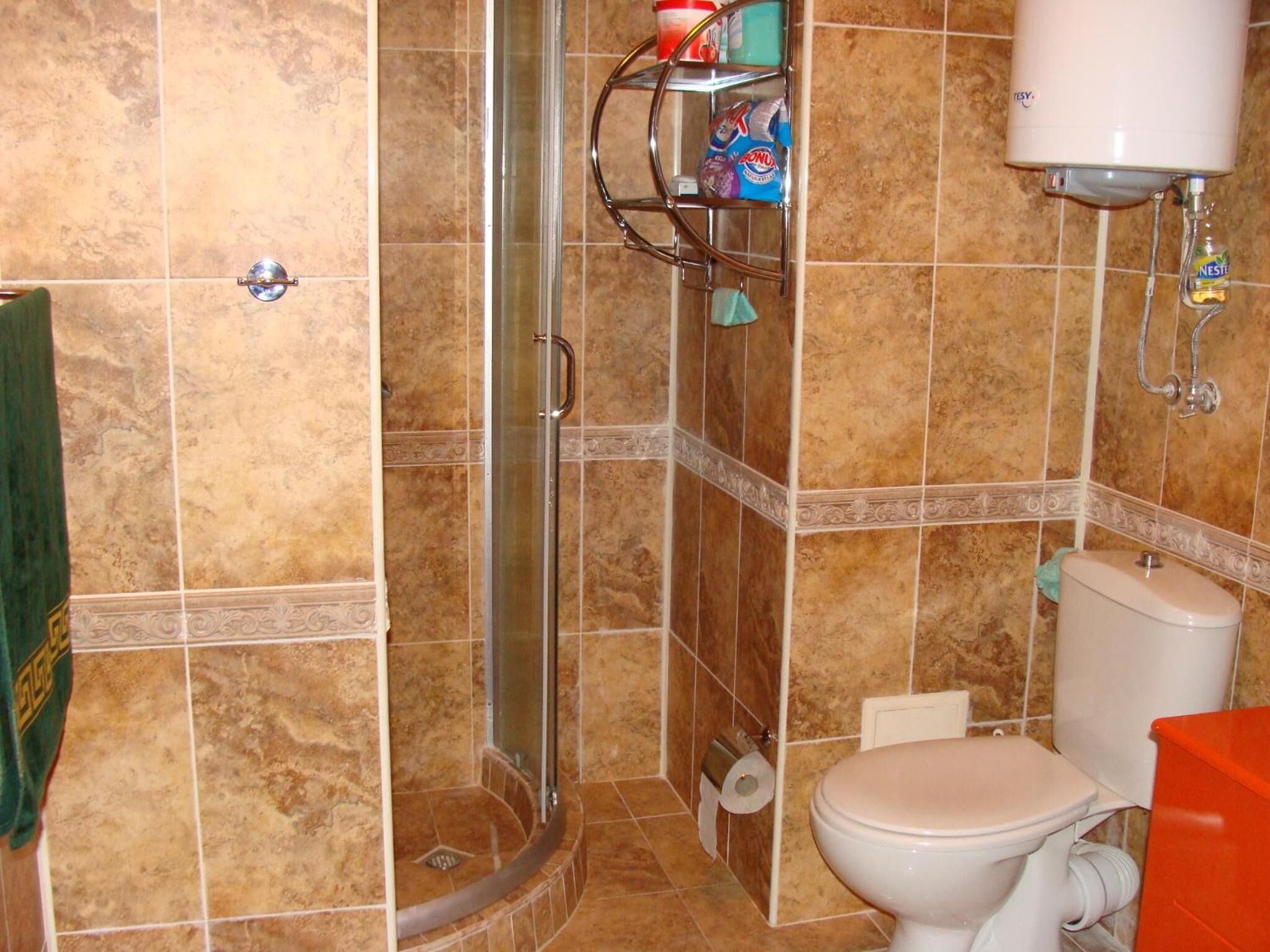 A bathroom with a shower, toilet, and a shelf with toiletries.