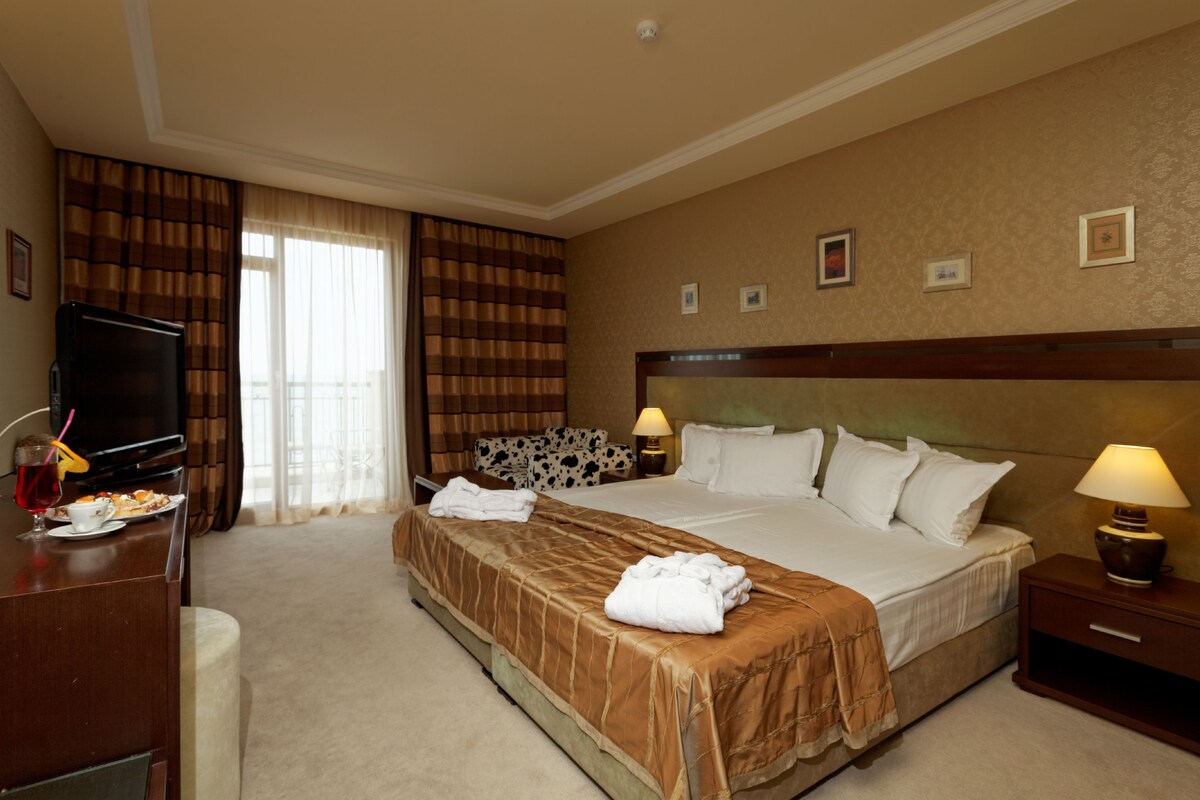 A hotel room with a bed, a TV, a desk with a lamp, and a window with curtains.