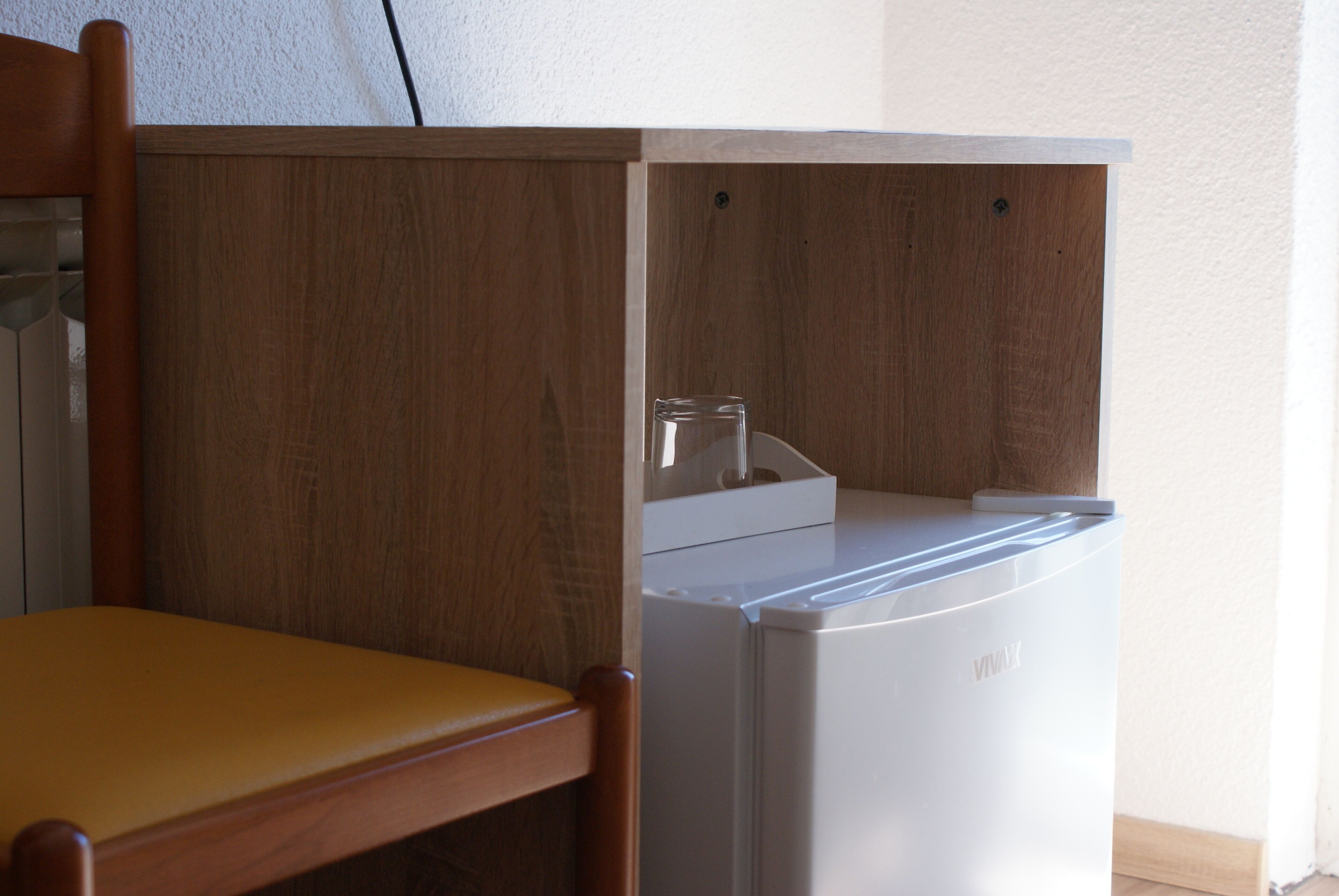 A kitchen area with a white refrigerator, wooden cabinets, and a wooden chair.
