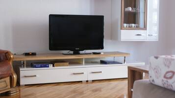 A living room with a flat-screen TV on a wooden stand, a white cabinet with glass doors, and a brown leather chair.